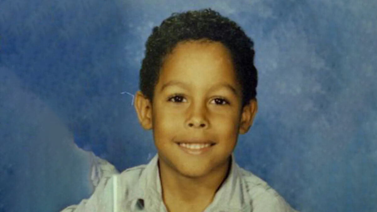 Young child criminal smiling in a portrait photo against a blue background, representing child criminals and disturbing acts.