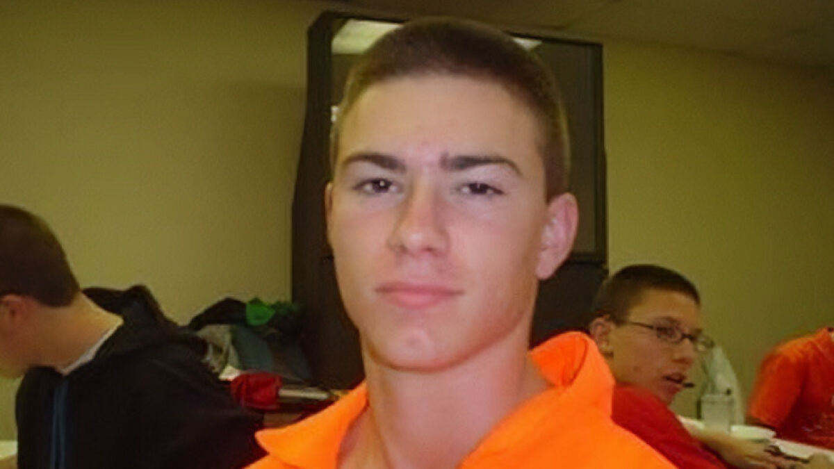 Young man in an orange shirt with peers in a room, related to momu2019s claim about skinned body in Las Vegas museum.