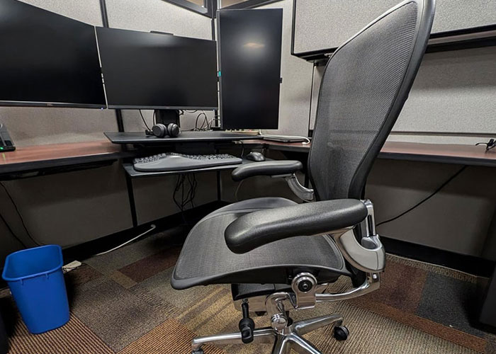 Ergonomic $1.8K office chair in a modern cubicle with multiple computer monitors and keyboard setup.