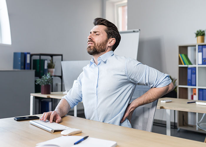 Man sitting in office chair rubbing his back, showing discomfort with his expensive $1.8K office chair at work.