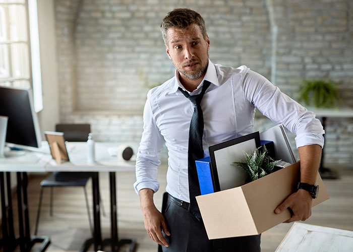 Man holding cardboard box with personal items, looking stressed after losing job over office chair dispute.