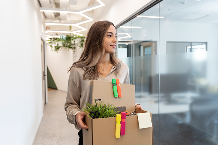 Young employee carrying a box of office items during an office swap, while leaving a modern workplace hallway. Young employee carrying a box of office items during an office swap, while leaving a modern workplace hallway.