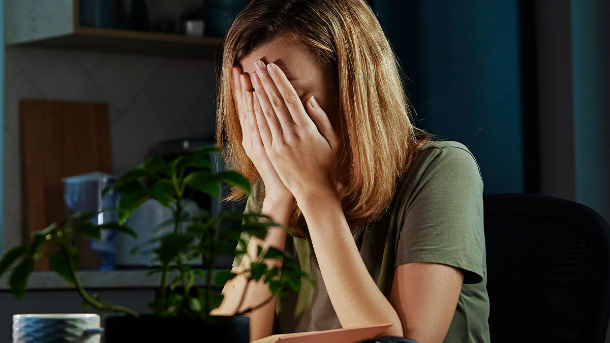 Frustrated coworker in office swap covers face in tears, stressed by employee taking everything during workspace change.