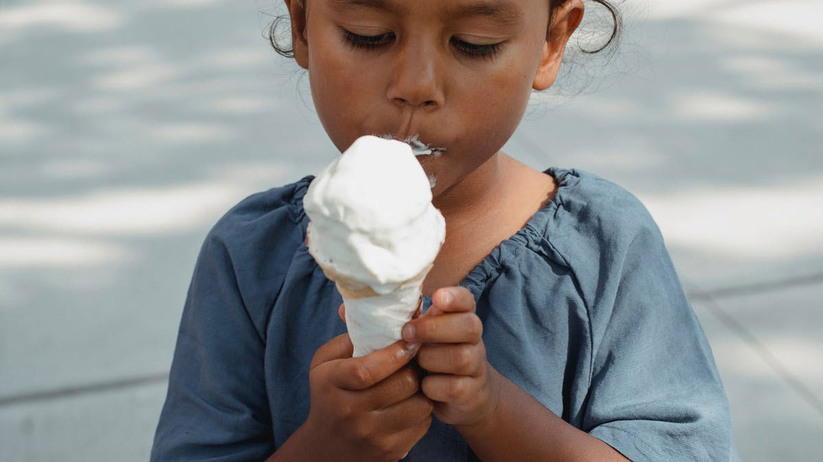 Child eating melting ice cream cone outdoors on a sunny day, unrelated to Karens examples or scary content.