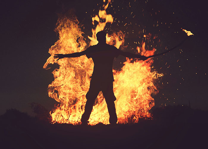 Silhouetted person standing with arms outstretched in front of large blazing fire, illustrating weird and crazy ER stories.
