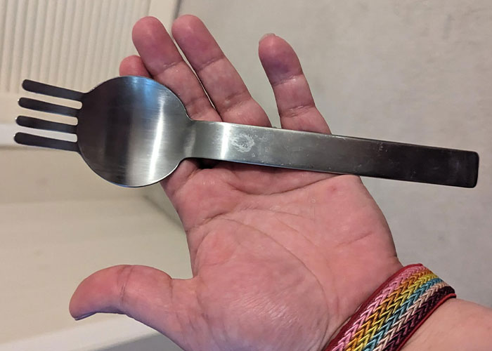 Hand holding a strange metal utensil with fork and spoon features, illustrating weird and crazy ER stories.