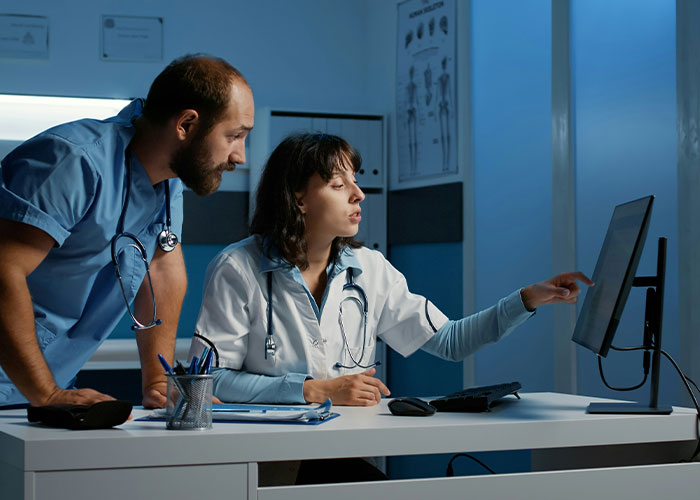 Two ER doctors in a dimly lit room reviewing patient data on a computer screen, discussing unusual emergency cases.