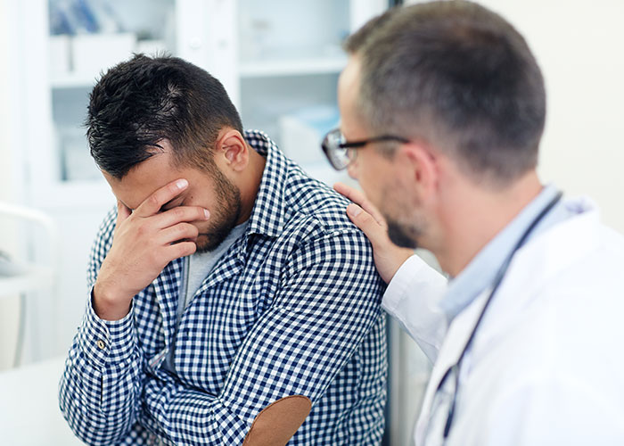 Man looking distressed while doctor in white coat offers support in a hospital, illustrating weirdest and craziest ER stories.