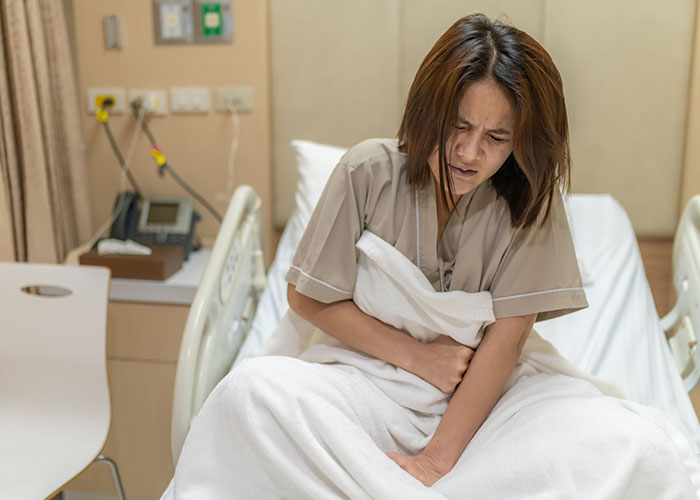 Woman in hospital bed clutching her abdomen in pain, illustrating one of the weirdest and craziest ER stories.