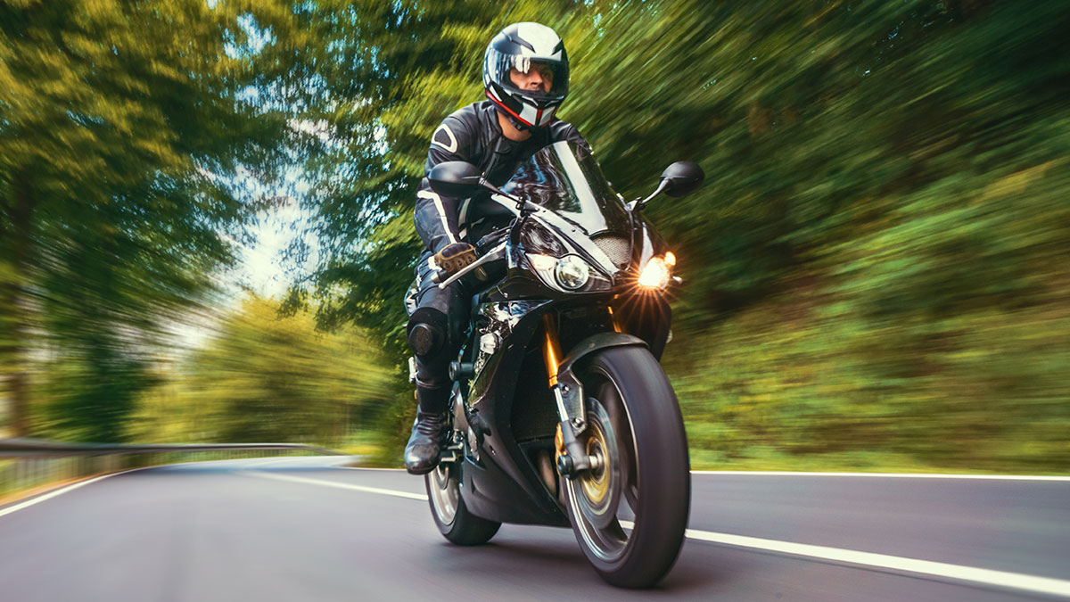 Motorcyclist wearing helmet riding at high speed on winding road surrounded by blurred trees, illustrating crazy ER stories.