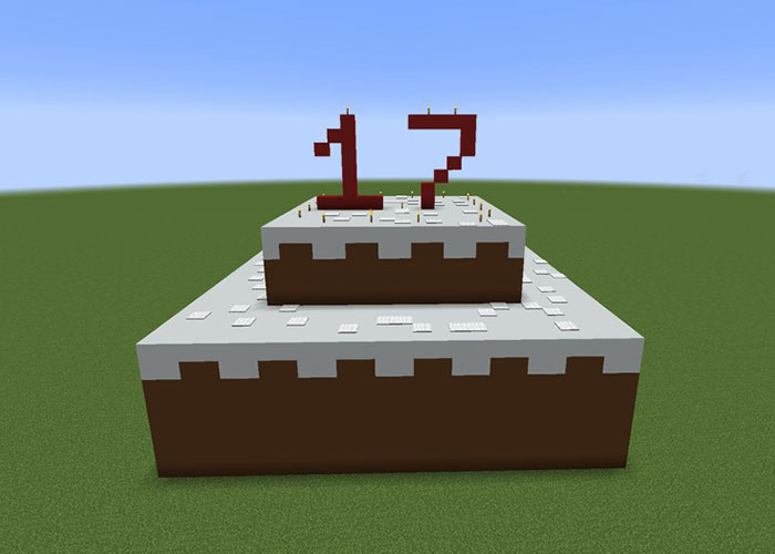 Minecraft-style pixelated birthday cake with red number 17 candles on flat grass under clear blue sky.