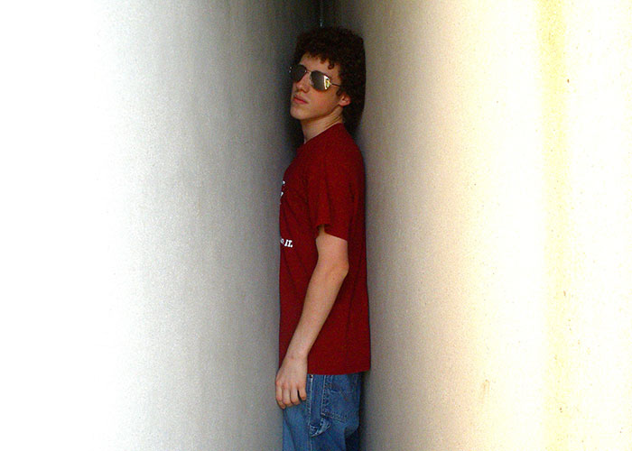 Teen wearing sunglasses and a red shirt standing closely between two narrow walls, illustrating narrowly avoided being kidnapped concept