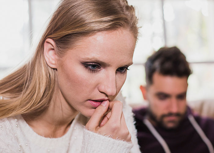 Worried woman looking down with a man blurred in the background, illustrating narrowly avoided being kidnapped scenario.