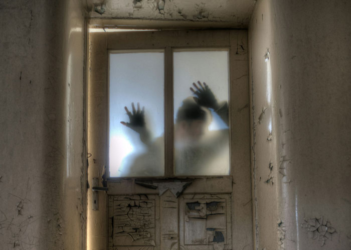 Silhouettes of two people pressing hands against frosted glass of a worn, c*****d door, evoking disturbing internet kidnapping threads.