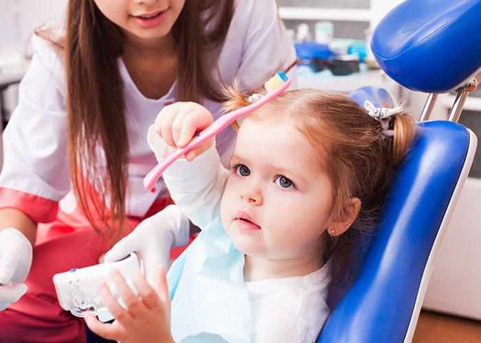 Young girl in dental chair holding a toothbrush, with a dentist assisting, illustrating narrowly avoided being kidnapped safety concept.