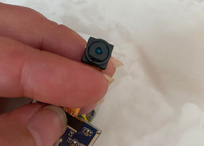 Close-up of a small hidden camera held between fingers, representing disturbing internet threads about narrowly avoided kidnapping.