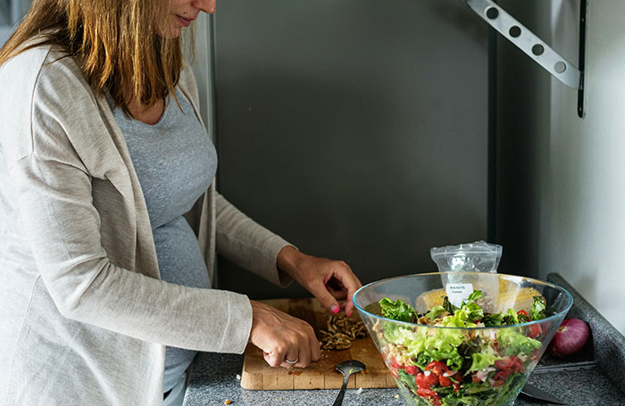 Pregnant woman preparing a healthy salad in the kitchen, emphasizing self-care and demanding husband respect.
