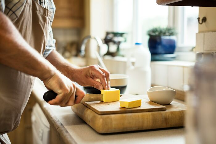 Home cook sharpening knives while cutting butter on a wooden board in a well-lit kitchen.