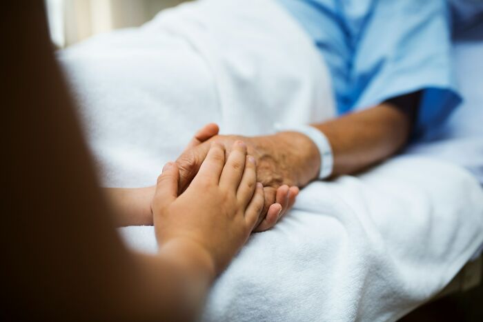 Person holding the hand of a patient in hospital bed, symbolizing heavy confessions and emotional support.