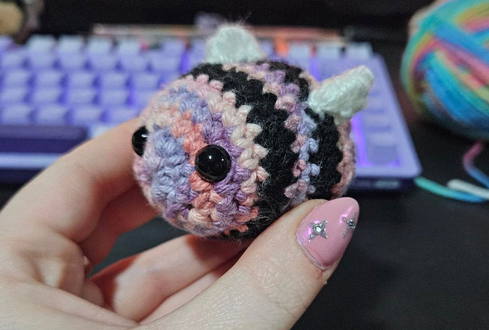 Hand holding a small striped crocheted bee with black button eyes, showcasing a proud crochet project close-up.