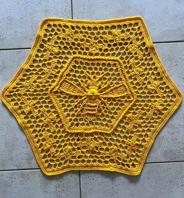 Yellow crochet doily with a bee pattern in the center, showcasing proud crochet enthusiasts' intricate handmade project.