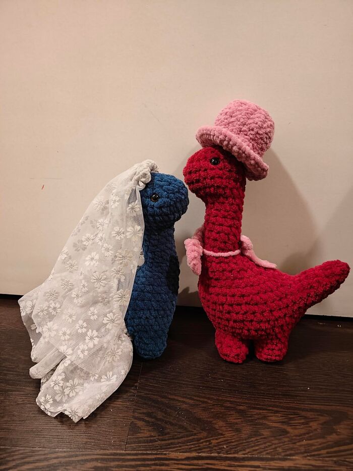 Two crocheted dinosaur figures dressed as bride and groom, showcasing proud crochet projects with detailed accessories.