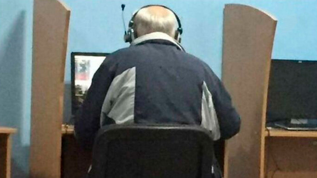 Elderly man wearing headphones gaming at a computer desk in a quiet room with gaming privacy panels.