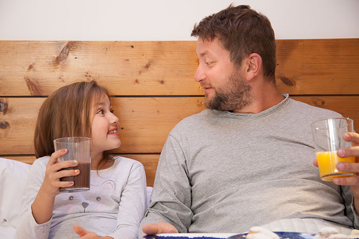 Teen and father sharing drinks and breakfast in bed, highlighting family dynamics and adoption concerns.