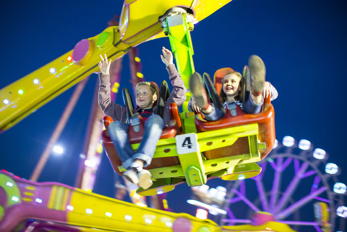 Two children enjoying a brightly lit amusement park ride at night, highlighting the power of water in thrilling experiences.