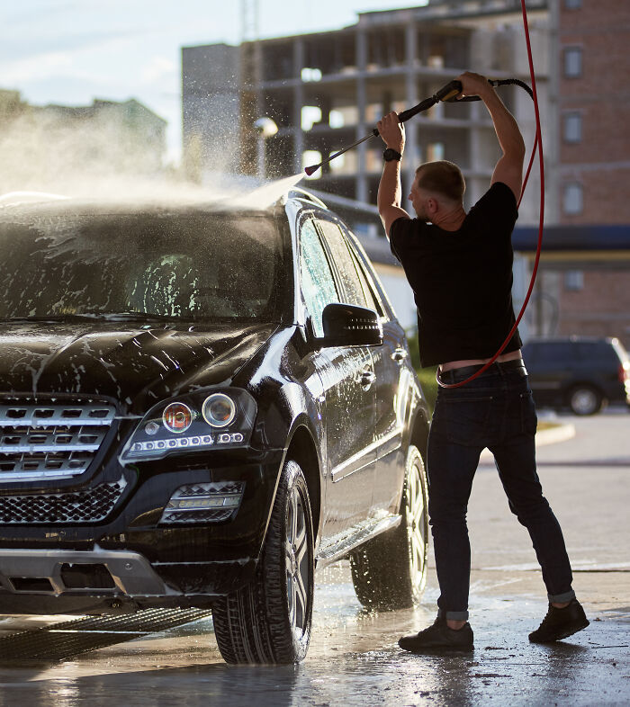 Man using a high-pressure water hose to wash a black SUV, demonstrating the powerful force of water in action.