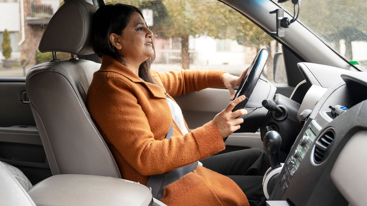 Woman driving a car wearing an orange coat and seatbelt, highlighting water dangers during rainy weather outside.