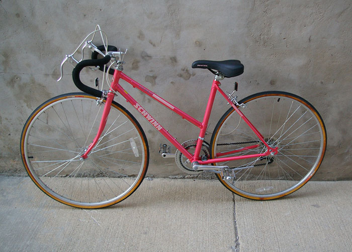 Vintage Schwinn road bike with drop handlebars and thin tires parked against a concrete wall for Corporate Darwin Award.