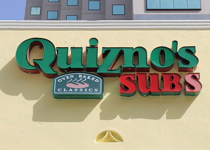 Quiznos Subs restaurant sign on a building representing companies competing for the corporate Darwin award.