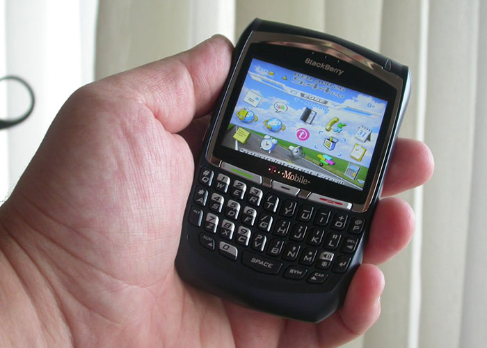 Hand holding an old Blackberry smartphone representing companies competing for the corporate darwin award.