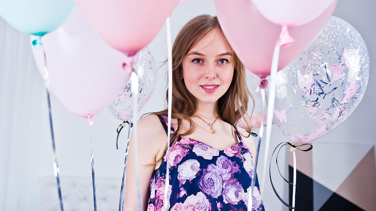 Teen girl at birthday party with pink and clear balloons reflecting a mean plan involving school invitation refusal