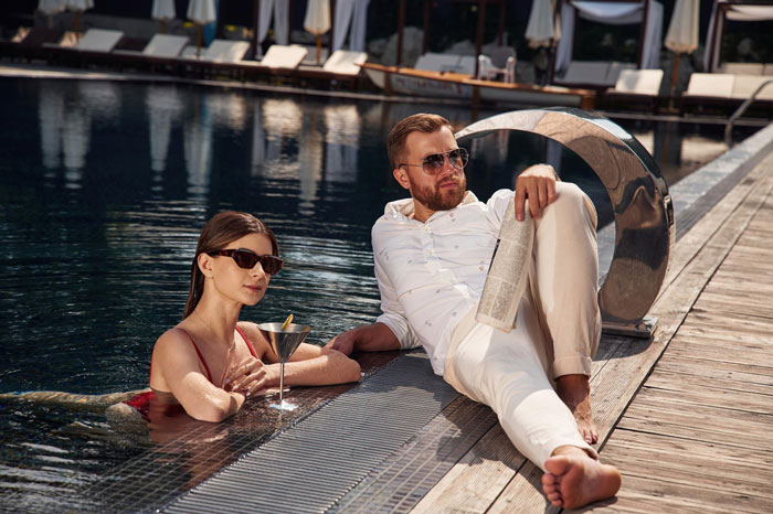 Young woman and man relaxing by the poolside, discussing daughter money surgeries while enjoying a cocktail on a sunny day. Young woman and man relaxing by the poolside, discussing daughter money surgeries while enjoying a cocktail on a sunny day.
