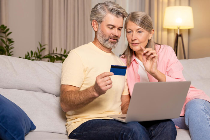 Middle-aged couple looking at a laptop and holding a credit card, discussing daughter money surgeries online. Middle-aged couple looking at a laptop and holding a credit card, discussing daughter money surgeries online.