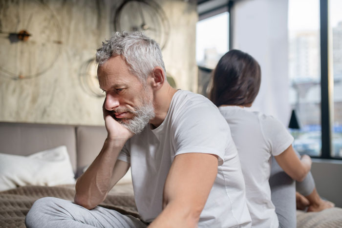 Man and woman sitting back to back on bed looking upset, reflecting tension over daughter money for surgeries decisions. Man and woman sitting back to back on bed looking upset, reflecting tension over daughter money for surgeries decisions.