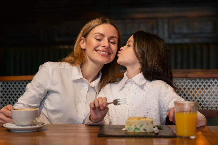 Woman and child sharing a moment at a cafe, with a plate of food and drink, highlighting foodie woman and kid relationship. Woman and child sharing a moment at a cafe, with a plate of food and drink, highlighting foodie woman and kid relationship.