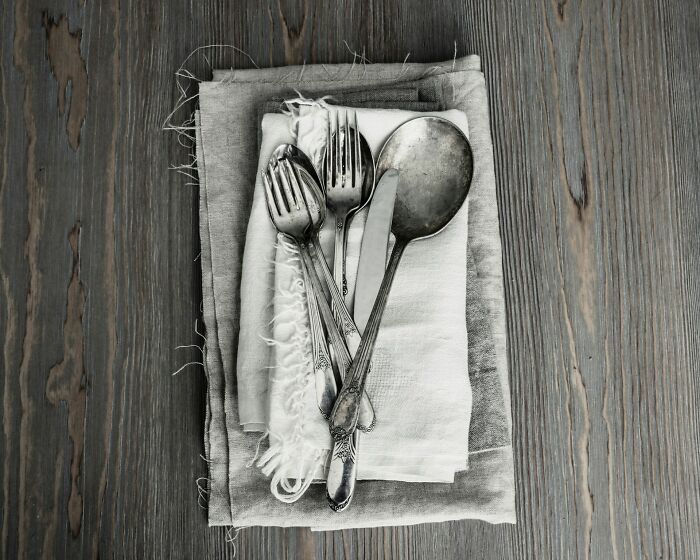 Stack of vintage silver cutlery on folded linen napkins over a wooden surface, symbolizing heavy confessions and untold stories.