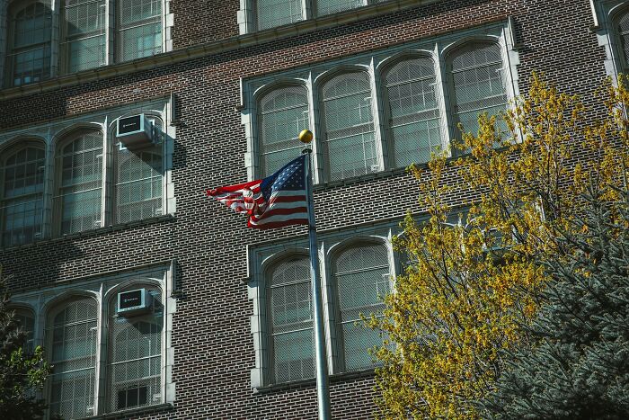 American flag waving on a pole outside a brick building with windows and trees, illustrating crazy coincidences experienced.