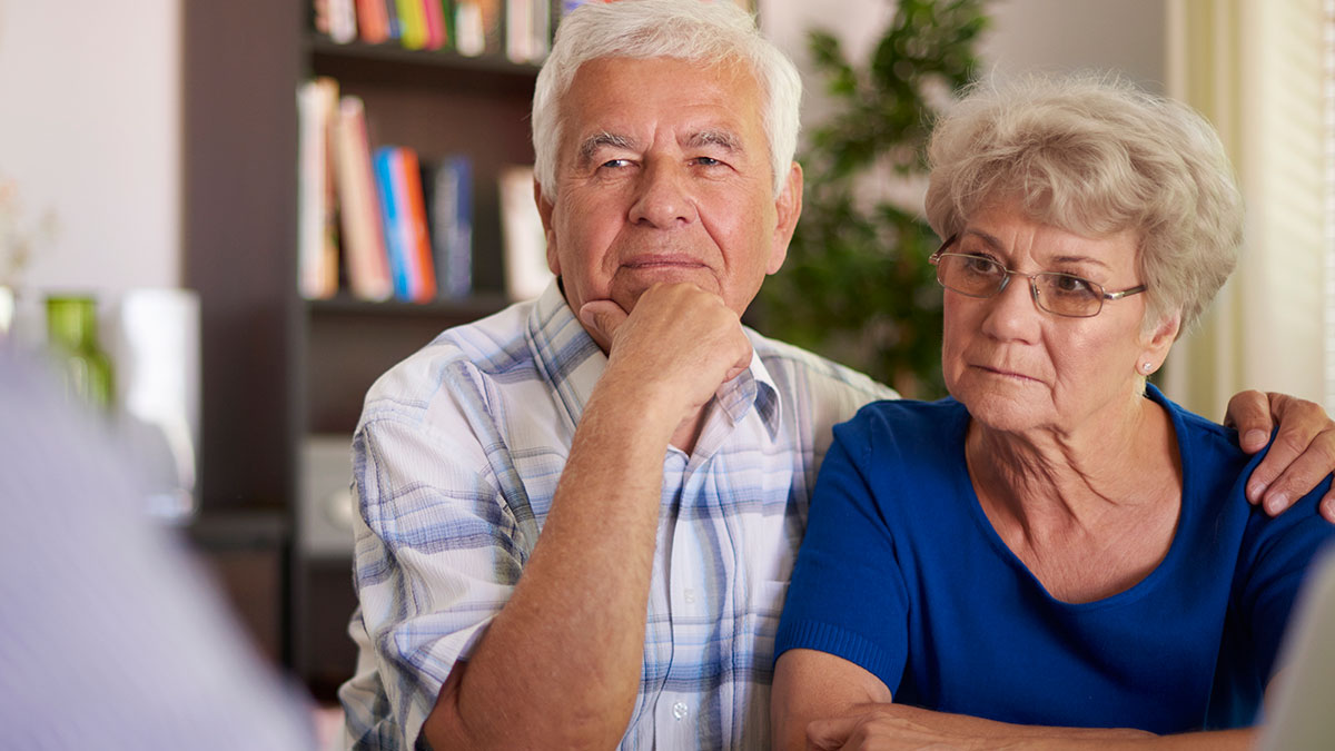 Elderly couple discussing wedding demands and prenup request from wealthy in-laws in a serious home setting.