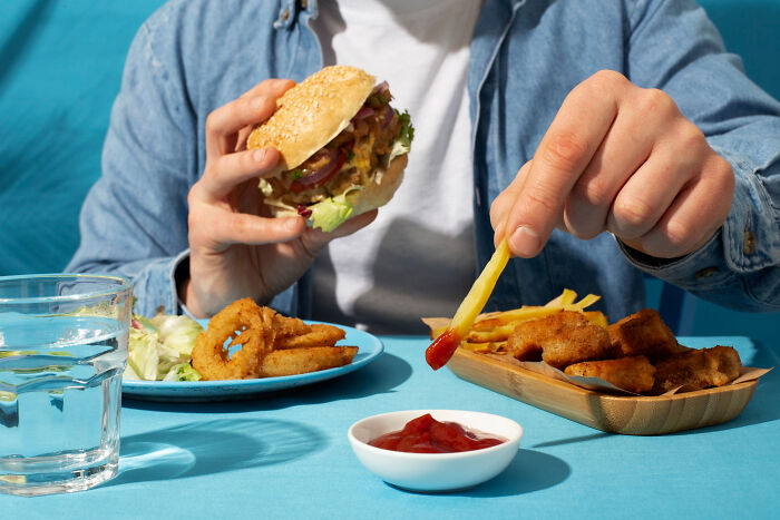 Person dipping french fries in ketchup while holding a burger, illustrating Dr Google versus real doctor meal choices.