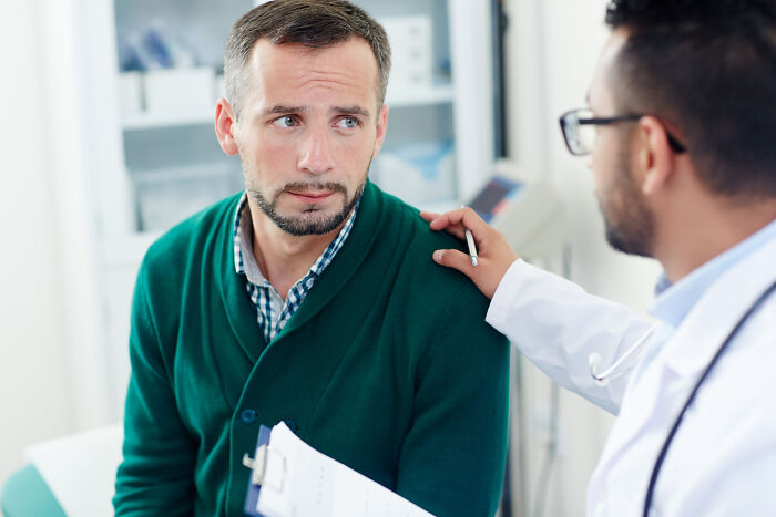 Doctor in white coat reassuring concerned male patient during medical consultation in clinic setting.