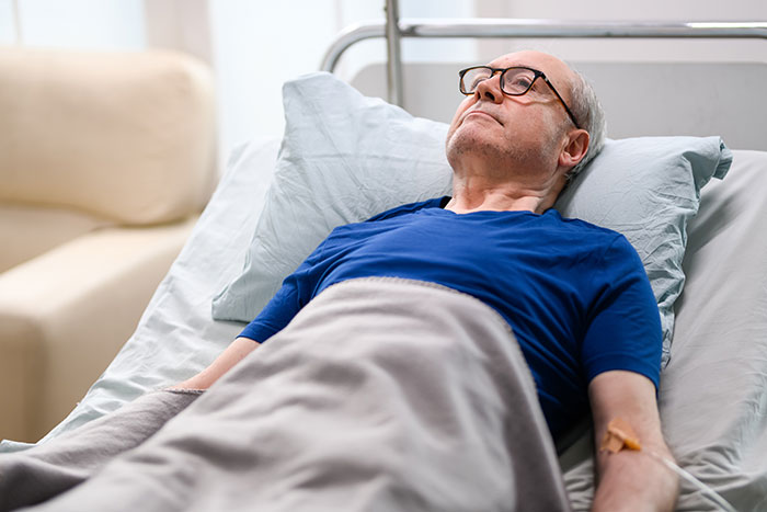 Elderly man wearing glasses lying in hospital bed with intravenous drip, illustrating doctors messed up cases.