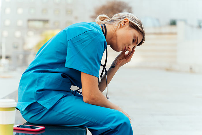 Female doctor in blue scrubs sitting outside looking stressed, illustrating moments doctors messed up bad.