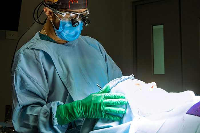 Surgeon wearing protective gear performing a procedure on a patient under bright surgical lights in an operating room.