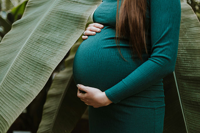 Pregnant woman in a green dress holding belly surrounded by large tropical leaves, illustrating doctors messed up bad risks.