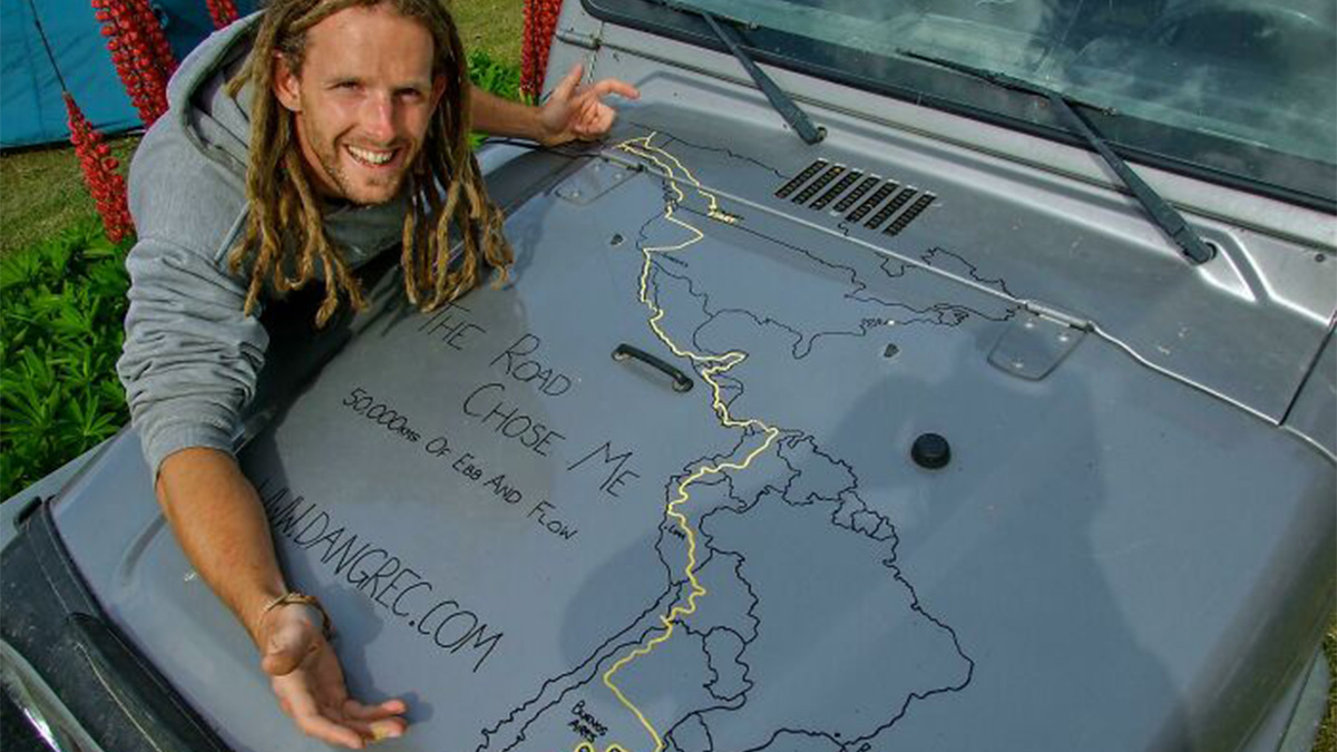 Man with dreadlocks smiling beside a car showing a detailed travel map, representing dreams turned into reality inspiration.