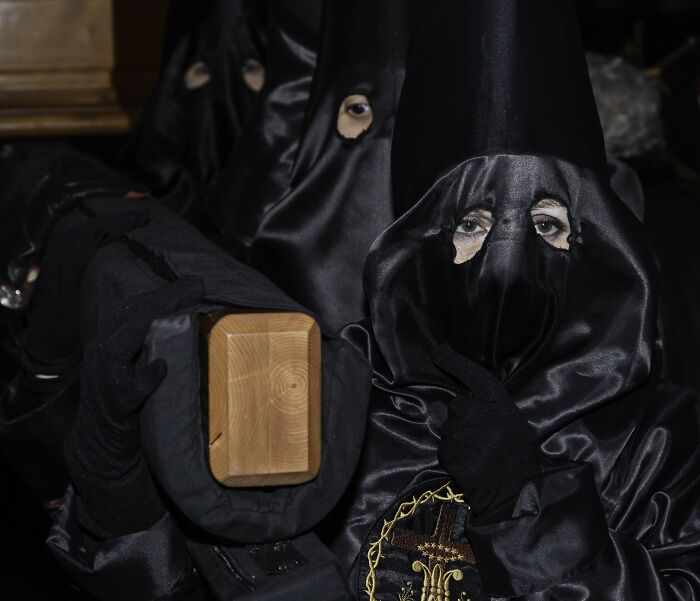 People wearing black satin robes and hoods with eye holes, representing dark internet rabbit holes taking over lives.